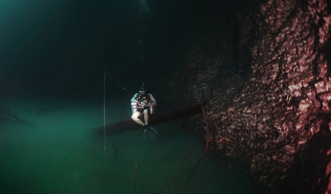 Một thợ lặn đang ngồi câu trên cành cây bắc ngang con sông nằm dưới đáy sông. Đây là một điều kỳ thú chỉ có ở Hang động Cenote Angelita, Mexico. Nó được gọi là dòng sông dưới đáy đại dương. Bởi sau 30m ở tầng nước ngọt trên cùng, lặn xuống tiếp 60m nước mặn mới có thể nhìn thấy dòng sông xanh thẳm này. Ở đây, nước lặng lẽ chảy như một màn sương ở dưới đáy sông.